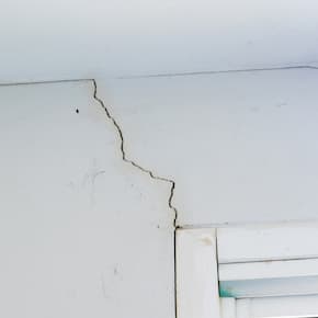 Close-up of a crack in a white wall near a window frame, indicating structural damage