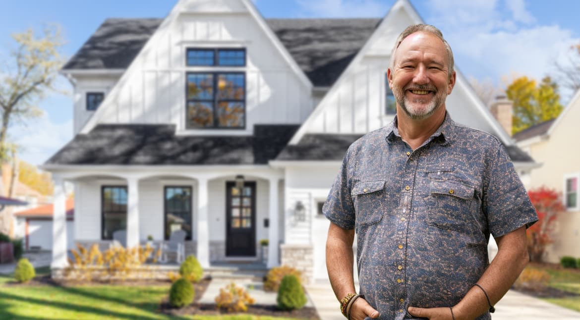 A smiling man standing in front of a beautiful white house with a well-maintained yard